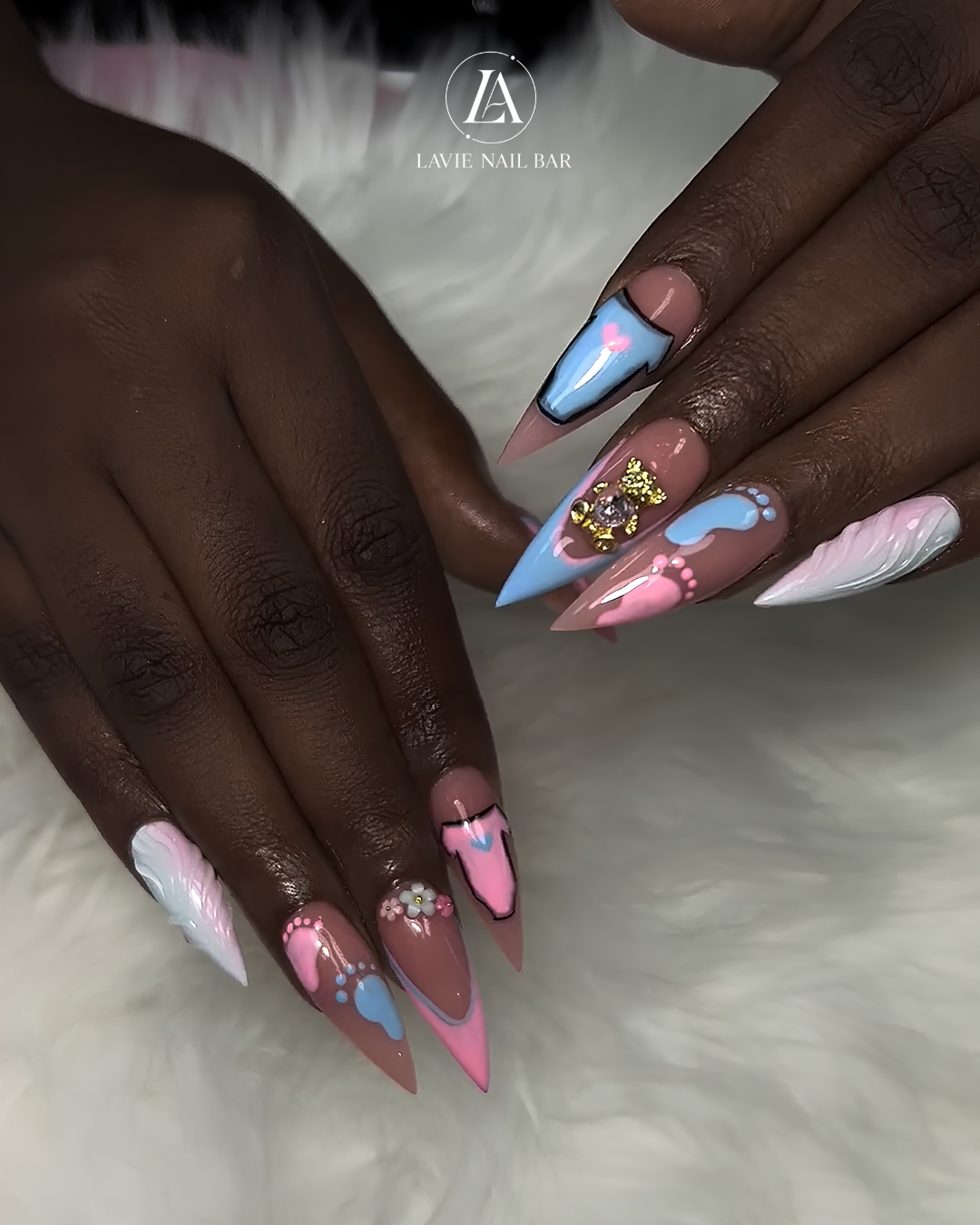 Baby shower stiletto nails in pink and blue with tiny footprints, a teddy bear charm, and 3D white swirls