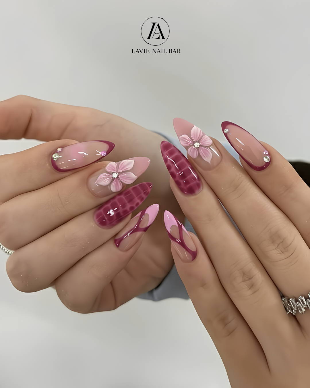 Almond nails with burgundy French tips, croc-print accents, and 3D pink flowers with rhinestone centers